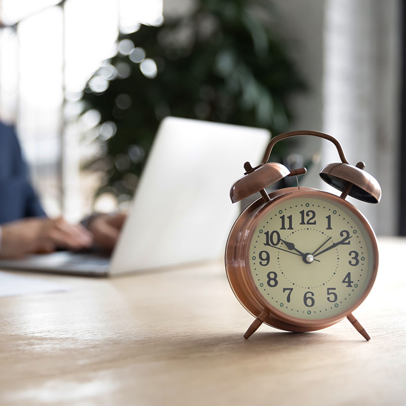 Mężczyzna pracujący przy laptopie. Na biurku stoi budzik